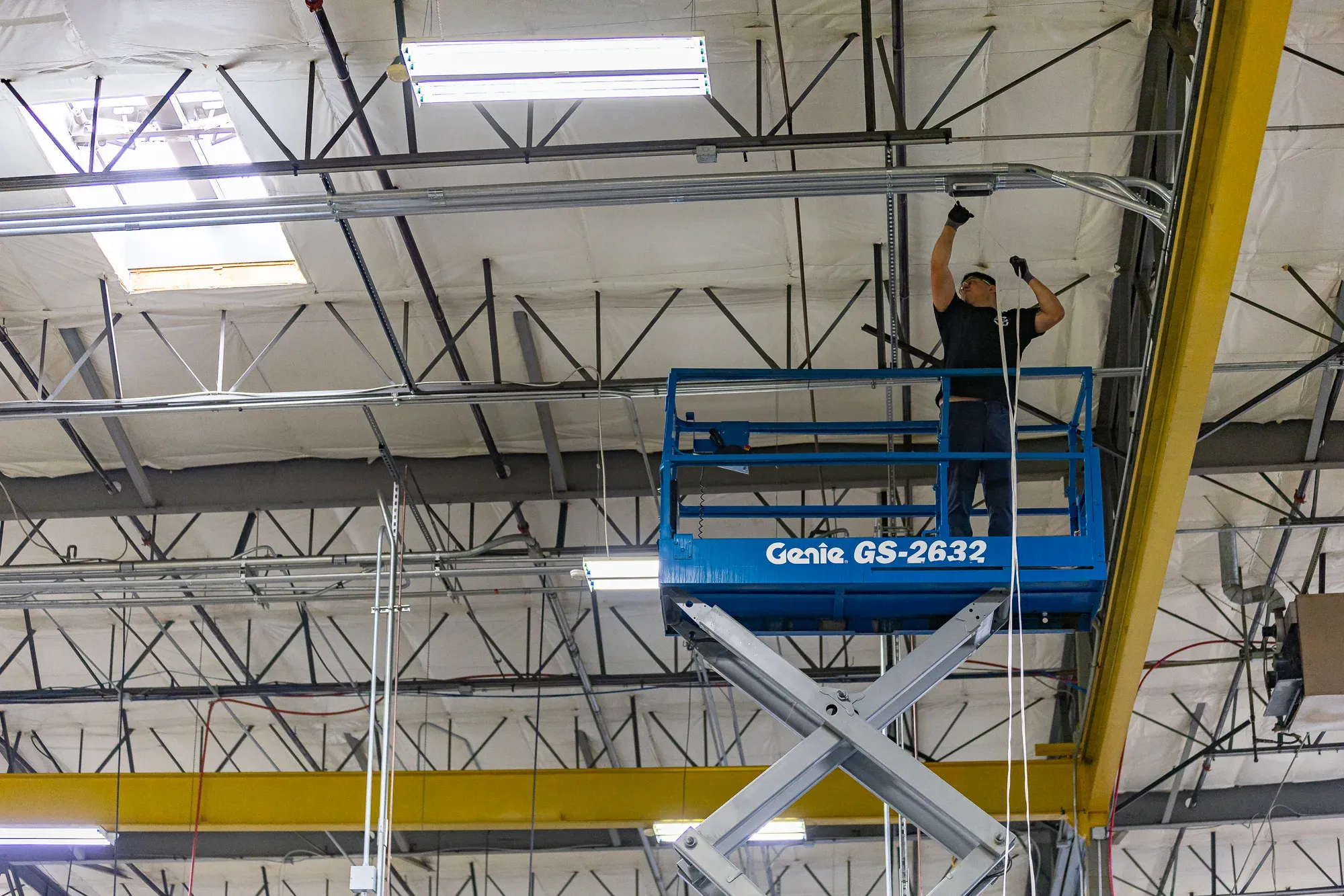 Electrician on scissor lift installing warehouse lighting