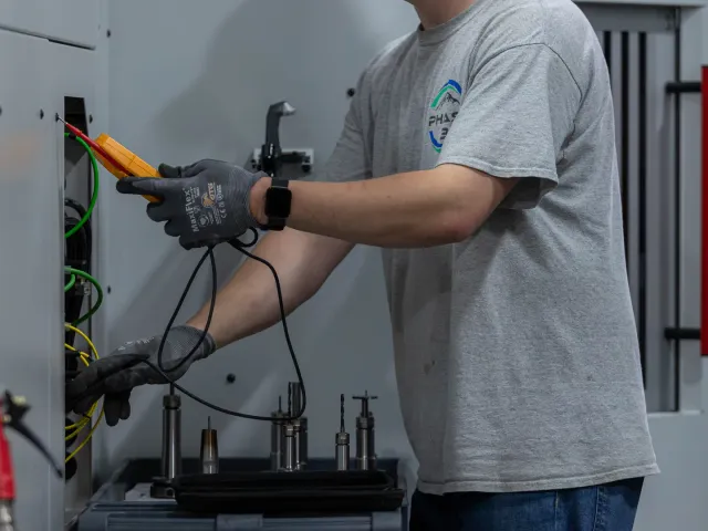 Industrial electrician testing CNC machine electrical connections with multimeter