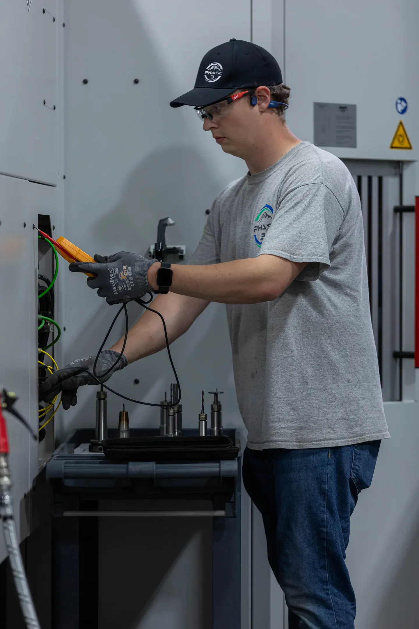 Industrial electrician testing CNC machine electrical connections with multimeter